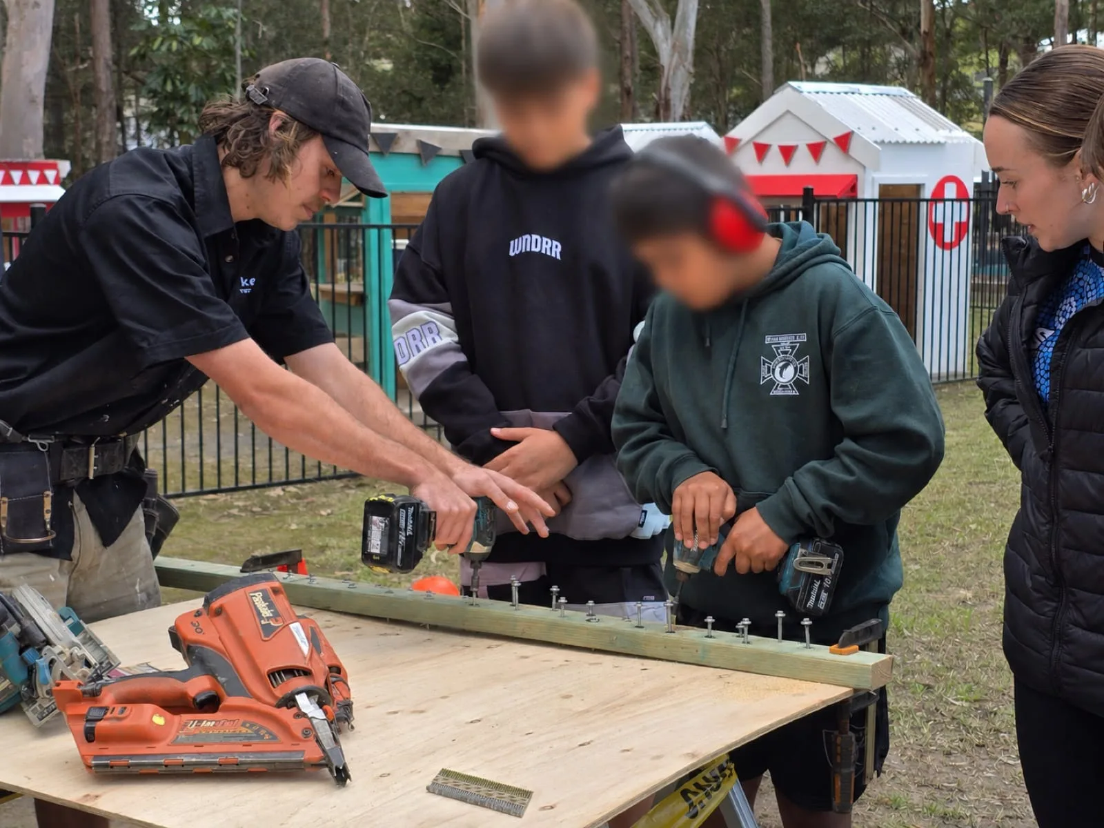 Akers Construction carpenter guiding a student through a power tool exercise at a school workshop